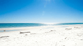 Strandtag scene, bright daylight, ocean view with sun glare reflecting on water and sand.