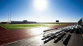 Feldsport scene, bright daylight, stadium bleachers and running track beside a green field.